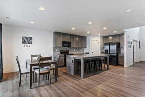 Kitchen featuring a kitchen bar, backsplash, black appliances, an island with sink, and dark wood-style flooring