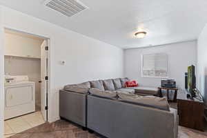 Carpeted living area with washer / dryer, tile patterned flooring, and a textured ceiling