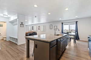 Kitchen with a center island with sink, a kitchen breakfast bar, open floor plan, light stone countertops, and light wood-style flooring
