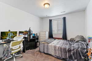 Carpeted bedroom with a textured ceiling and an office area
