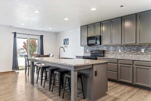 Kitchen featuring tasteful backsplash, light stone countertops, a kitchen island with sink, black appliances, and recessed lighting