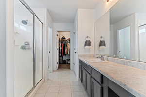 Full bath featuring a stall shower, light tile patterned floors, a spacious closet, and vanity