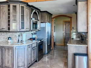 Kitchen featuring arched walkways, tasteful backsplash, glass insert cabinets, vaulted ceiling, and light stone counters