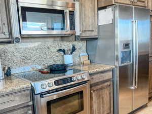 Kitchen featuring stainless steel appliances, decorative backsplash, light stone counters, and light tile patterned floors