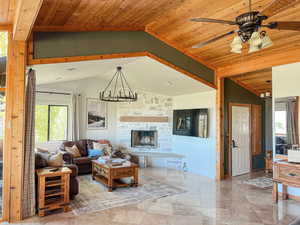 Living room with healthy amount of natural light, a chandelier, a stone fireplace, wood ceiling, and a ceiling fan