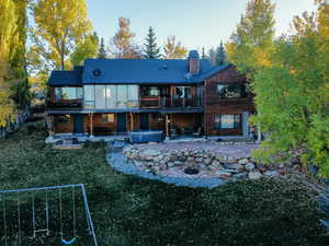 Back of house with a patio area, a jacuzzi, a yard, a chimney, and a balcony