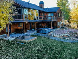 Rear view of property with a hot tub, a patio, a chimney, a balcony, and a lawn