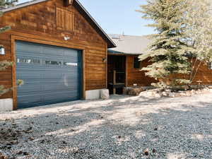 Rustic home with a garage, roof with shingles, and gravel driveway