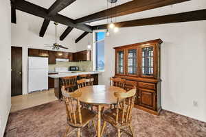 Dining area featuring high vaulted ceiling, beamed ceiling, light carpet, and a ceiling fan