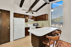 Kitchen featuring a peninsula, white appliances, dark brown cabinetry, light countertops, and a breakfast bar area