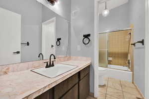 Full bath with bath / shower combo with glass door, light tile patterned flooring, and vanity