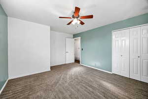 Unfurnished bedroom with dark carpet, a closet, and a ceiling fan
