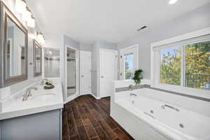 Bathroom featuring a whirlpool tub, double vanity, a shower stall, wood finish floors, and recessed lighting