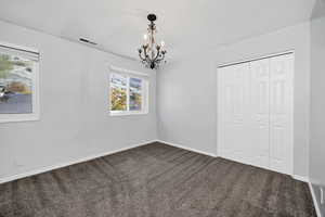 Unfurnished bedroom featuring dark carpet, a closet, and a chandelier