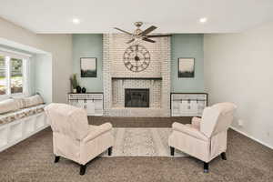 Carpeted living room with a brick fireplace, ceiling fan, and recessed lighting