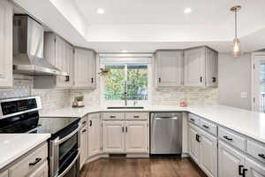 Kitchen with appliances with stainless steel finishes, wall chimney range hood, dark wood finished floors, hanging light fixtures, and recessed lighting