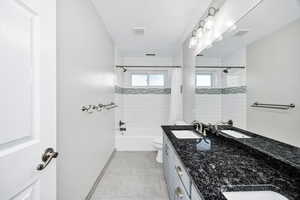 Bathroom featuring double vanity, shower / bath combo, and light tile patterned floors
