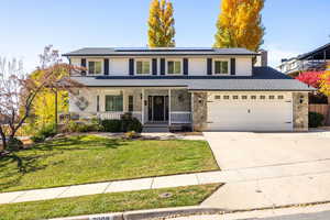 Traditional home with a porch, stone siding, driveway, and a garage