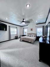 Carpeted primary bedroom with a textured ceiling, ceiling fan, multiple windows, and crown molding
