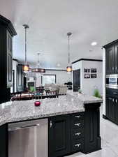 Kitchen with dark cabinetry, light stone counters, stainless steel appliances, pendant lighting, and light marble finish flooring