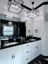 Full bath with a marble finish shower, double vanity, ornamental molding, and a chandelier