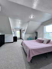 Bedroom with a textured ceiling, carpet flooring, and vaulted ceiling