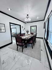 Formal dining room featuring light marble finish floors, ornamental molding, a textured ceiling, and a chandelier
