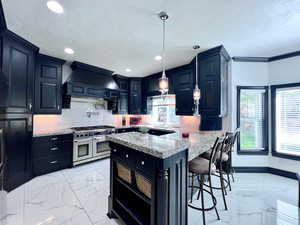 Kitchen featuring light marble finish flooring, light stone countertops, dark cabinetry, a kitchen breakfast bar, and double oven range