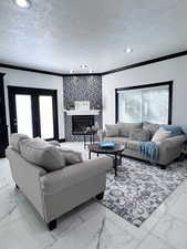 Living room featuring a textured ceiling, crown molding, healthy amount of natural light, marble finish flooring, and a glass covered fireplace