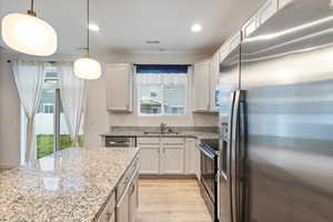 Kitchen with stainless steel appliances, hanging light fixtures, light wood-type flooring, light stone countertops, and recessed lighting