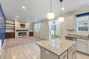 Kitchen featuring hanging light fixtures, light wood-style flooring, light stone counters, open floor plan, and a fireplace