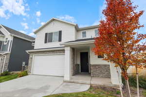 View of front facade with stone siding, a porch, an attached garage, and concrete driveway