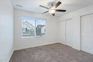 Unfurnished bedroom with carpet floors, two closets, and a ceiling fan