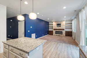 Kitchen featuring light stone countertops, light wood-type flooring, a kitchen island, pendant lighting, and recessed lighting