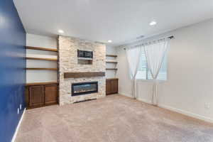 Unfurnished living room with light colored carpet, a stone fireplace, recessed lighting, and built in features