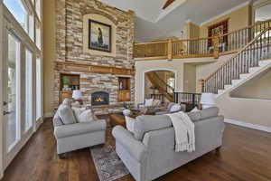 Living room featuring stairway, healthy amount of natural light, a fireplace, dark wood finished floors, and a towering ceiling