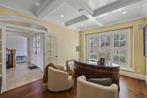 Home office with arched walkways, ornamental molding, beamed ceiling, coffered ceiling, and wood finished floors