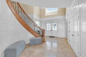 Entryway with a towering ceiling, stairway, a decorative wall, french doors, and tile patterned floors