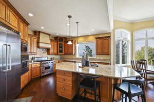 Kitchen featuring brown cabinetry, a kitchen bar, built in appliances, decorative light fixtures, and recessed lighting