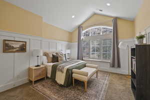 Carpeted bedroom featuring a decorative wall, vaulted ceiling, recessed lighting, and wainscoting