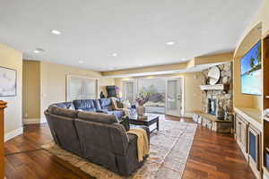 Living room with a fireplace, dark wood-type flooring, and recessed lighting