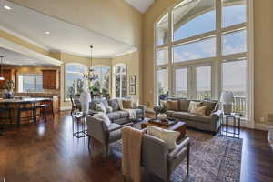 Living room featuring a chandelier, dark wood finished floors, crown molding, recessed lighting, and a towering ceiling