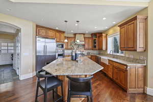 Kitchen featuring brown cabinetry, a kitchen breakfast bar, a kitchen island, built in appliances, and hanging light fixtures