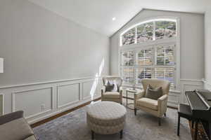Living area featuring lofted ceiling, a decorative wall, a wainscoted wall, and wood finished floors