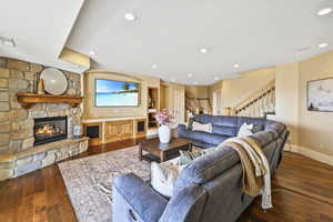 Living area with stairway, a stone fireplace, dark wood-type flooring, and recessed lighting
