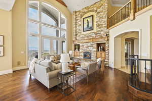 Living room with arched walkways, a fireplace, dark wood-type flooring, a towering ceiling, and crown molding