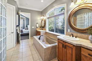 Ensuite bathroom featuring two vanities, light tile patterned floors, a whirlpool tub, ornamental molding, and recessed lighting