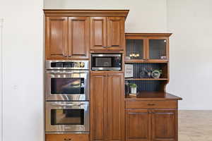 Kitchen with stainless steel appliances, dark countertops, brown cabinets, and glass insert cabinets