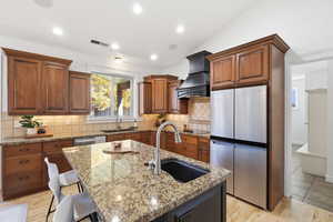 Kitchen with light wood-type flooring, appliances with stainless steel finishes, a kitchen breakfast bar, a center island with sink, and light stone countertops