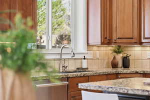 Kitchen featuring brown cabinets, backsplash, stainless steel dishwasher, and light stone counters